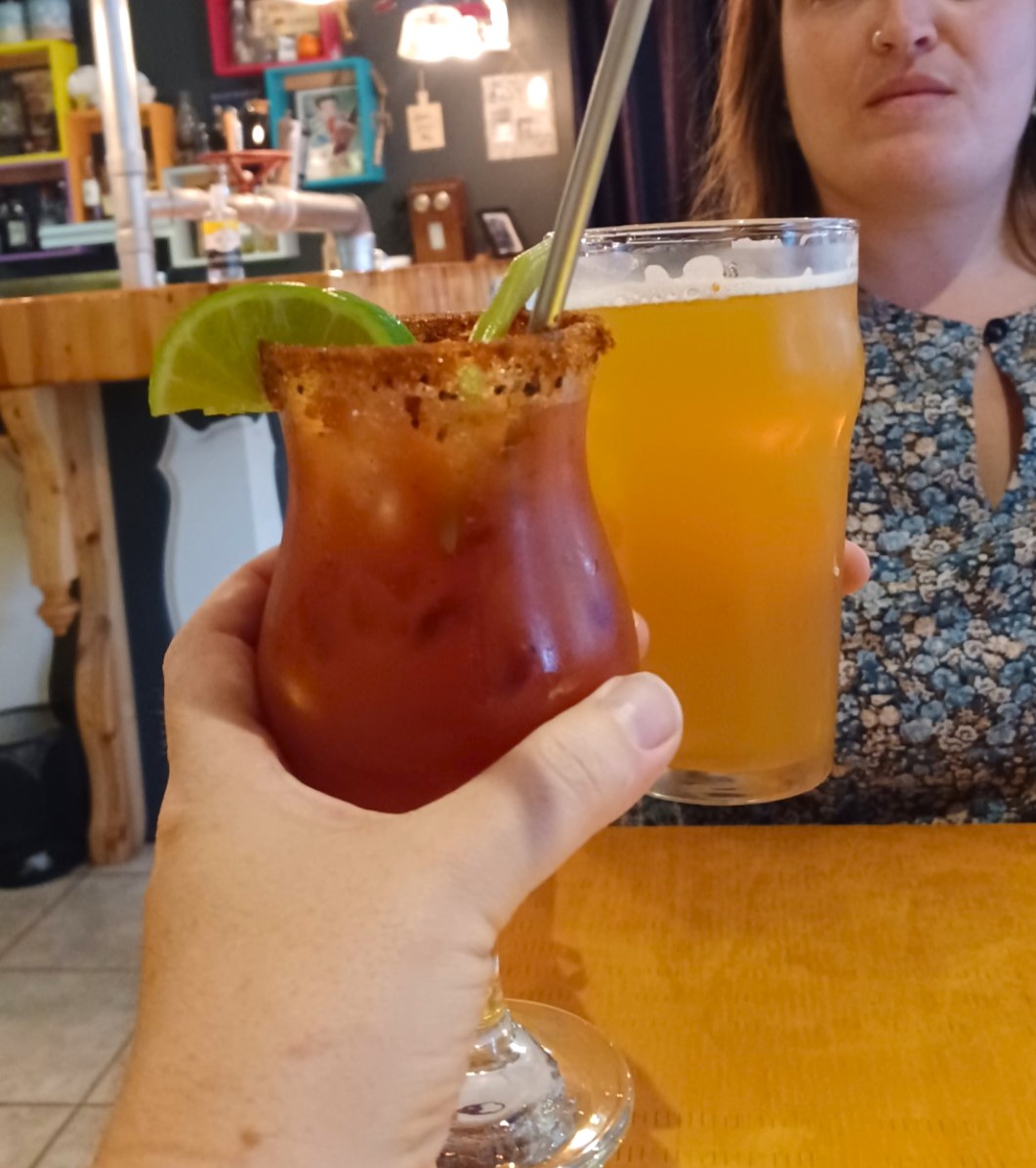 Une main tien un cocktail rouge et une autre personne tient un verre de bière. Les deux breuvages se rencontrer, comme pour faire un "santé". L'image a été prise au Ste-Anne, un restaurant de Ville-Marie, au Témiscamingue.